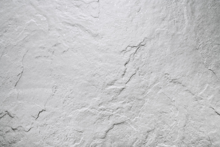 Light gray textured stone surface with subtle cracks and natural patterns, giving it a slightly rough and uneven appearance.